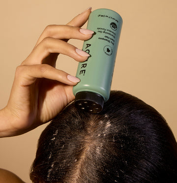 Woman applying dry shampoo directly to her scalp, focusing on hair freshness and quick styling